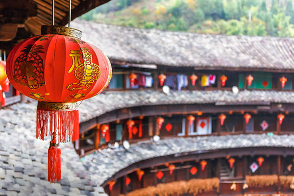 View along the wooden gallery and roof tiles of a Fujian Tulou with red, chinese lantern in the foreground.